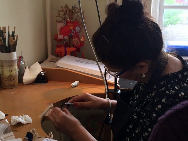 Shelanu member drills a hole in the pendant for a necklace
