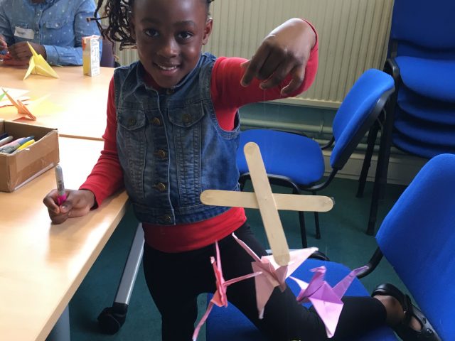 Child from ASIRT group proudly showing their finished origami crane
