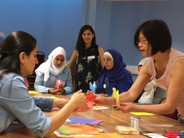 Shelanu member teaching Refugee Action clients how to fold origami cranes