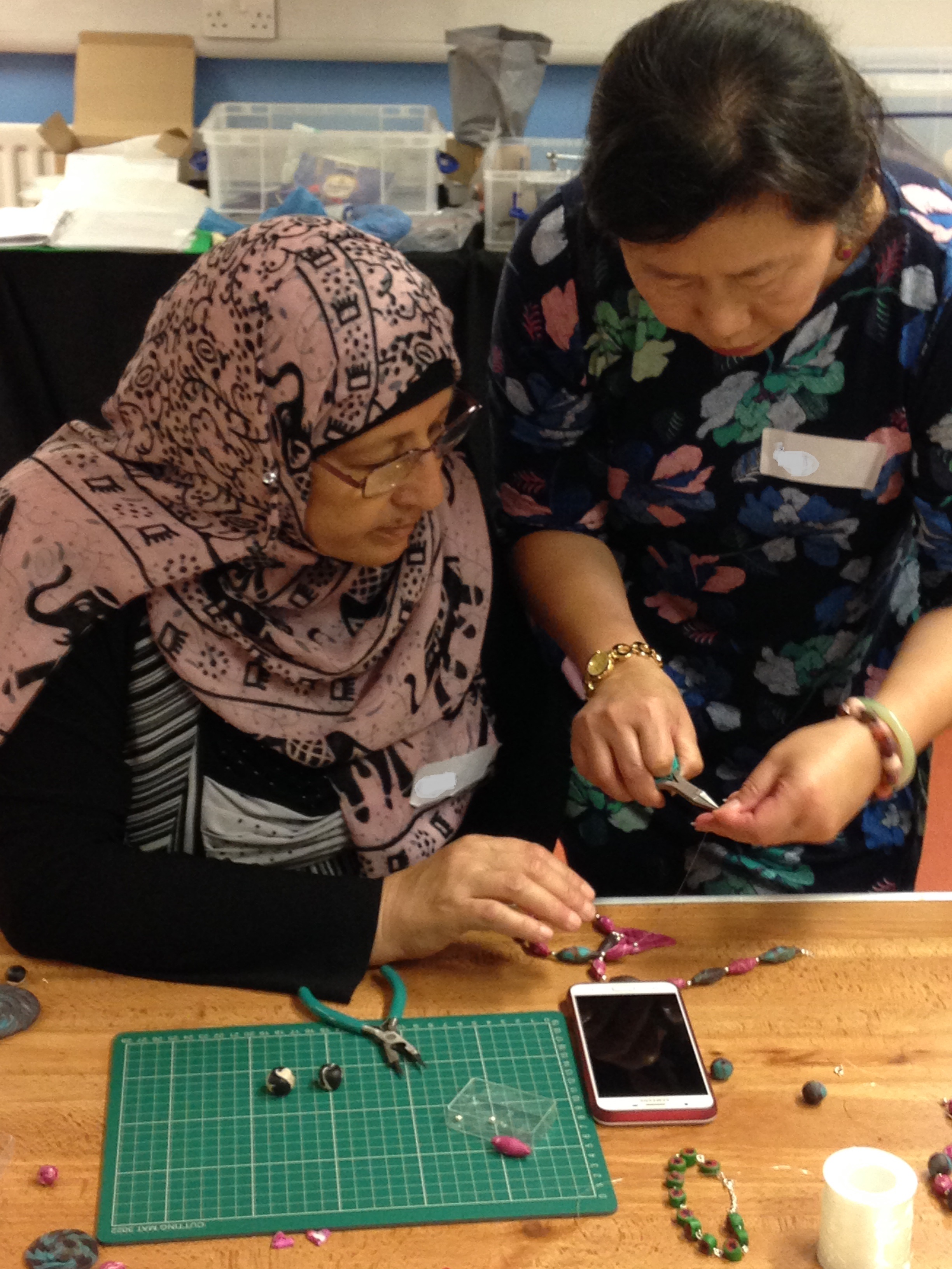 Shelanu member helps Refugee Action client at Refugee Action client bending the pearl eyelet.