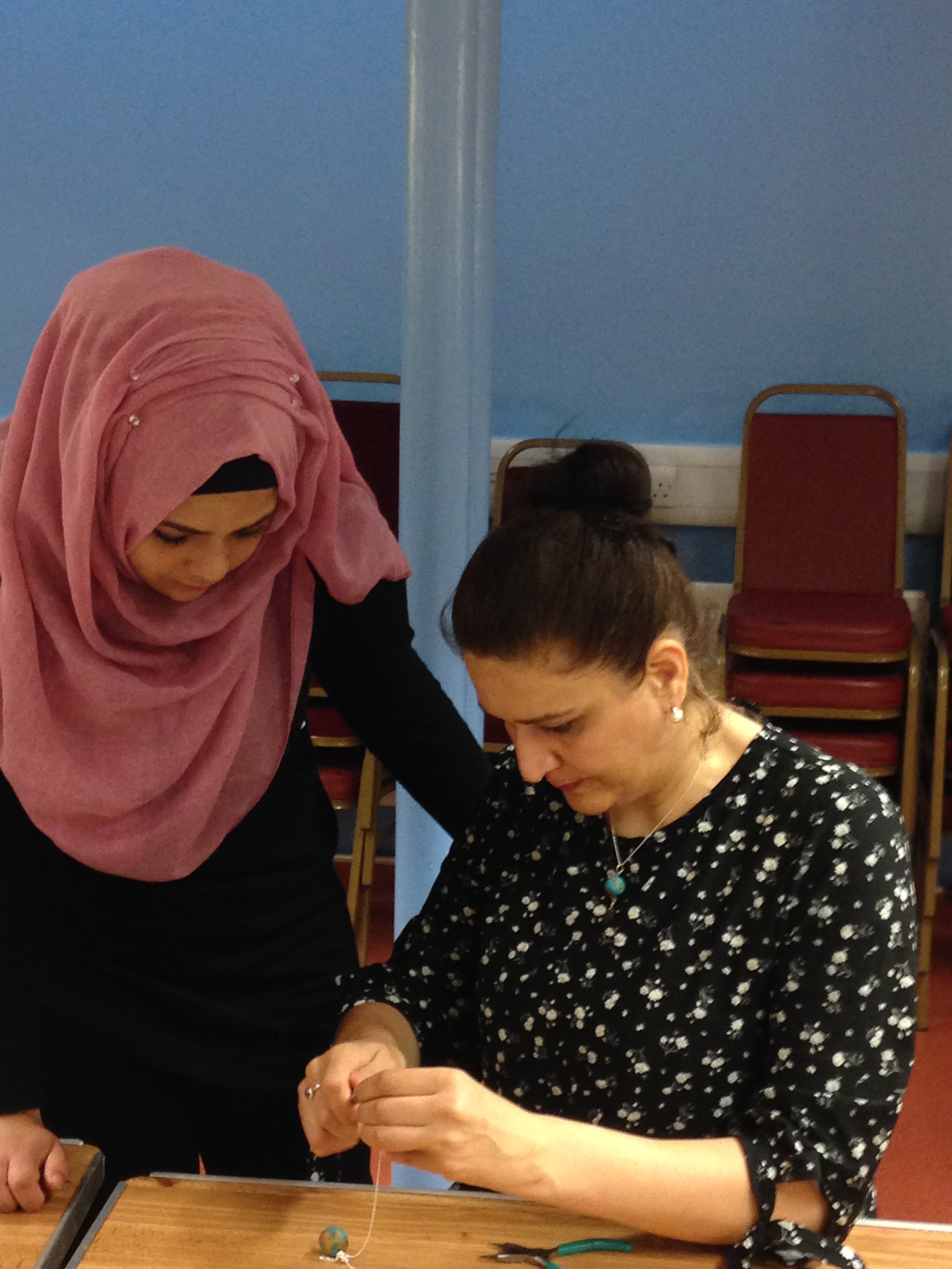 Shelanu member helping Refugee Action client to unravelling the pearls for her necklace.