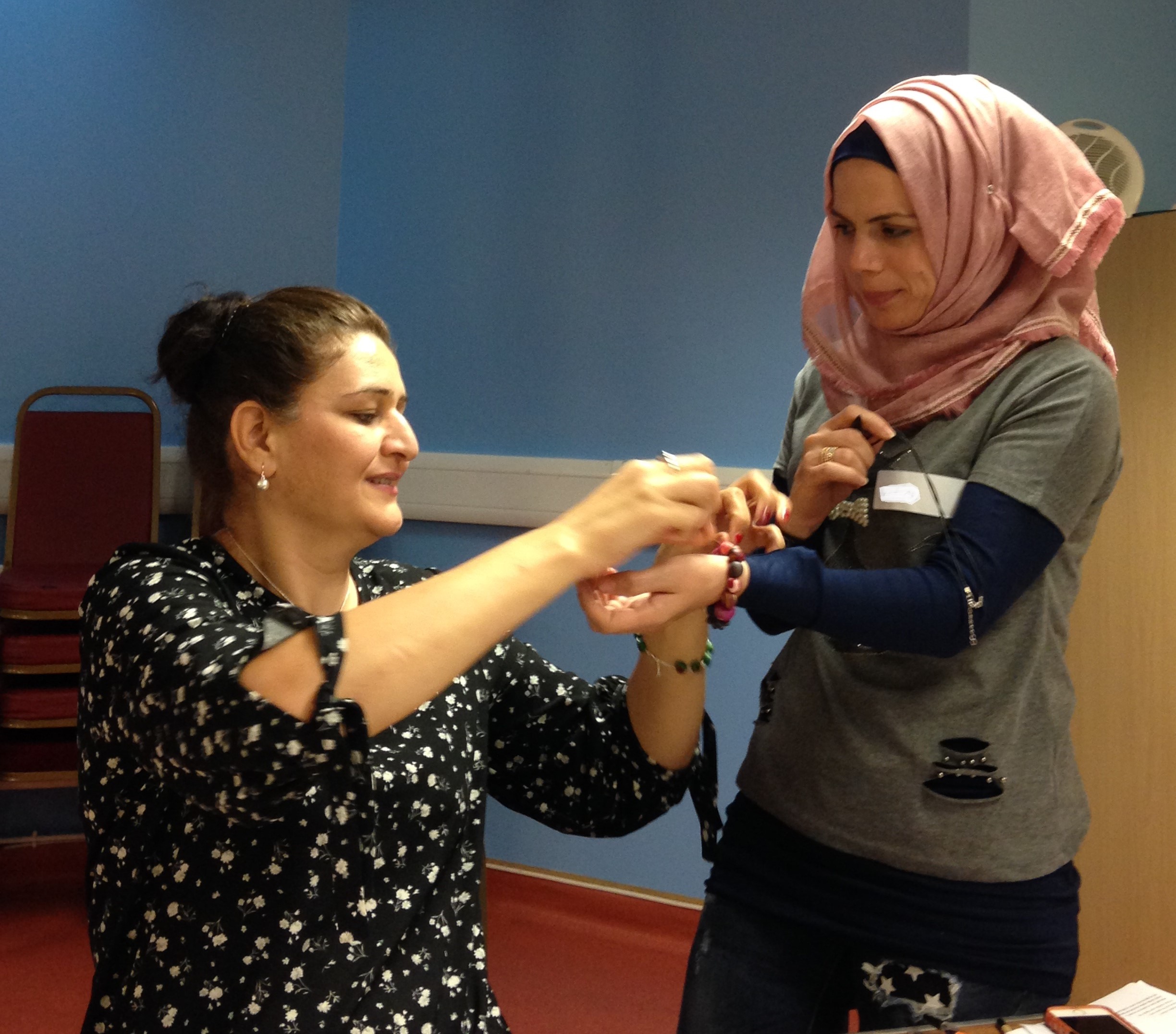 Shelanu member helps Refugee Action client to close her pink bracelet
