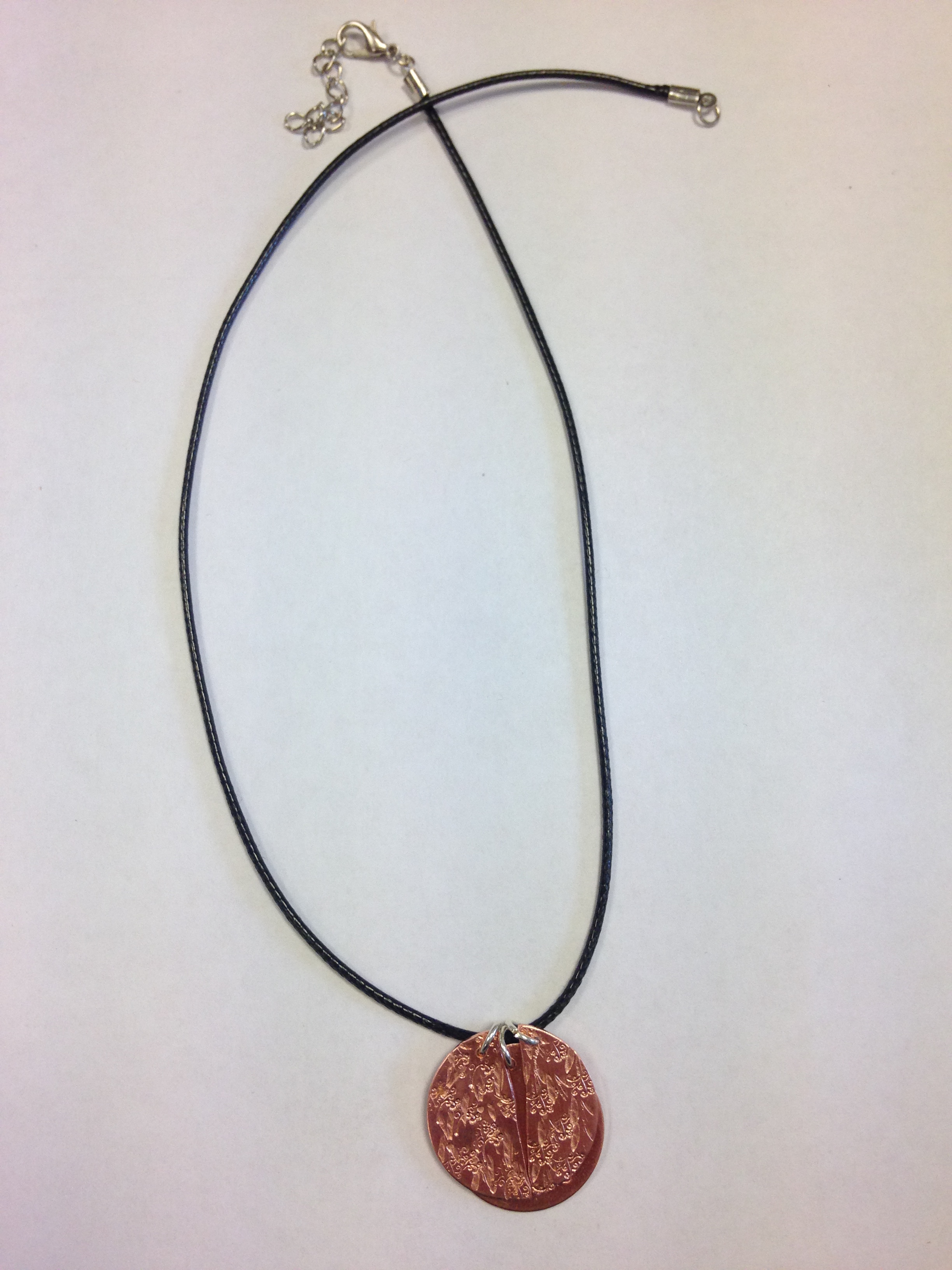 A necklace on whose copper disc a woman stamped a pattern.