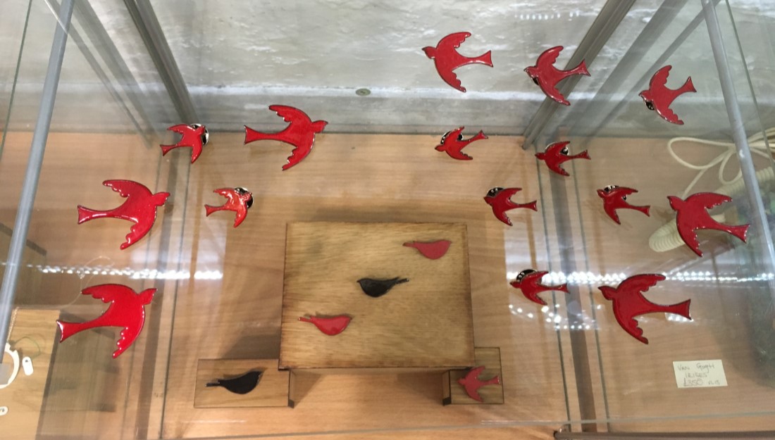 shelanu red enamel swallow bird brooches displayed in a flight formation on glass shelf